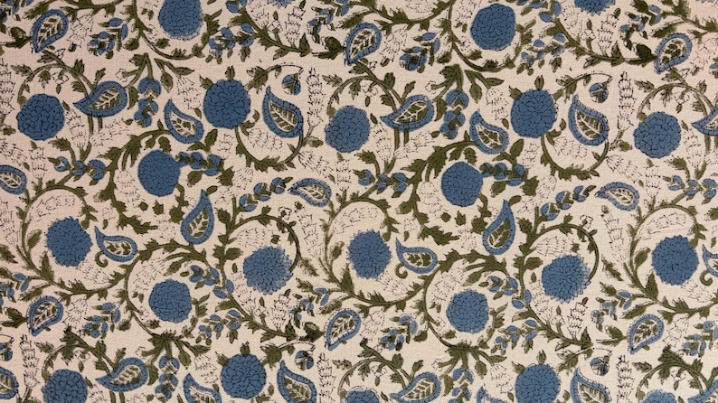 May include: Cream-colored fabric with a repeating pattern of blue floral and paisley shapes, connected by green vines and leaves. The design has a hand-blocked print appearance, creating a textured look.