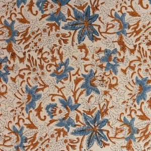 Peut inclure: Tissu crème avec un motif floral répétitif. Le motif présente des fleurs bleues avec des pétales détaillés et des tiges et feuilles marron. Le fond a une texture subtile et pointillée.
