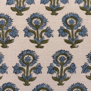 May include: Close-up of a fabric with a repeating floral pattern. The design features stylized blue flowers with green stems and leaves against a cream-colored background. The fabric has a textured appearance.