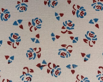 May include: Cream-colored fabric with a repeating pattern of blue and maroon roses and small triangular shapes. The floral design is evenly spaced across the textile, creating a visually appealing and balanced composition.