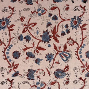 Puede incluir: Tela floral con un patrón repetitivo de flores y hojas azules y rojas sobre un fondo crema. El diseño presenta flores y follaje estilizados, creando un textil decorativo clásico.