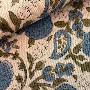 May include: Close-up of a fabric with a repeating floral pattern. The design features blue and green floral elements on a cream-colored background. The fabric is folded, showing the texture and pattern details.