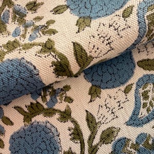 May include: Close-up of a folded fabric with a floral pattern. The design features large blue flowers and green leaves on a cream-colored background. The fabric has a textured appearance.