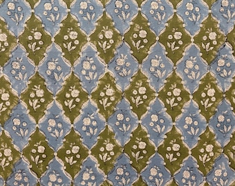 May include: A repeating pattern of blue and olive green diamond shapes, each containing a white floral design. The pattern is symmetrical and creates a textured, decorative effect, suitable for textiles or wallpaper.