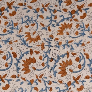 May include: Close-up of a fabric with a repeating floral pattern. The design features orange flowers and blue vines on a cream-colored background. The fabric has a textured appearance, suggesting a natural fiber.