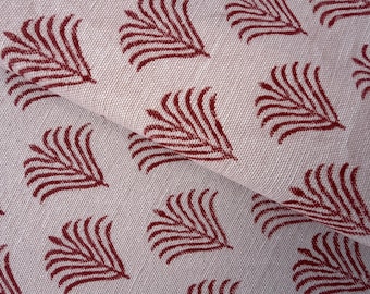 May include: Close-up of a folded fabric with a repeating pattern of maroon-colored stylized leaf designs. The fabric has a light beige background and a textured appearance, suggesting a linen or cotton material. The leaf pattern is evenly spaced.