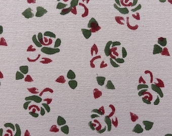 May include: Close-up of a fabric with a repeating floral pattern. The design features green and red stylized roses and leaves on a light beige background. The fabric has a textured appearance.