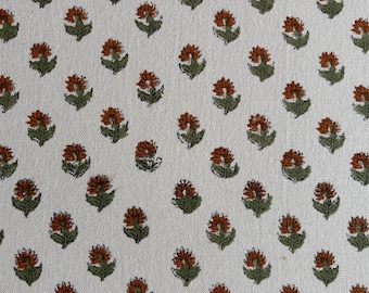 May include: A repeating pattern of small, stylized flowers on a white background. The flowers are a rusty orange color with green leaves. The fabric has a slightly textured appearance.