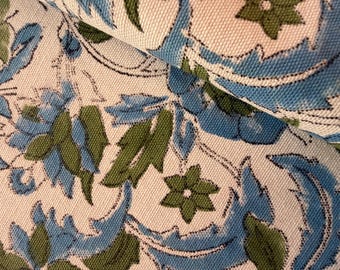 May include: Close-up of a fabric with a floral pattern. The design features blue and green leaves and flowers on a cream-colored background. The fabric is folded, showing the texture and detail of the print.
