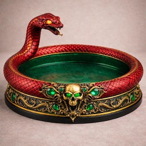 Può includere: Una ciotola decorativa rossa a forma di serpente con interno verde. La ciotola presenta una testa di serpente dettagliata e una base ornata da un teschio dorato e gemme verdi. Un pezzo unico di arredamento per la casa.