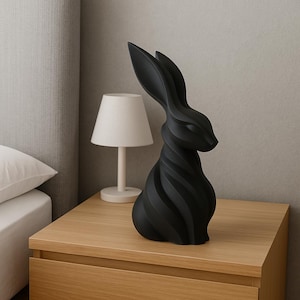 May include: A black rabbit sculpture with a spiral design. The decorative figurine is placed on a wooden nightstand next to a small white lamp. The rabbit has long ears and a detailed, textured body.