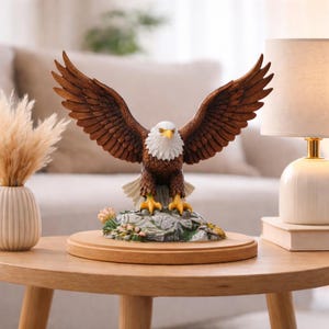 Puede incluir: Figura detallada de un águila calva americana con las alas extendidas. El águila tiene plumas marrones, cabeza blanca y pico y garras amarillas. Se alza sobre una base rocosa con flores, montada sobre una base redonda de madera.