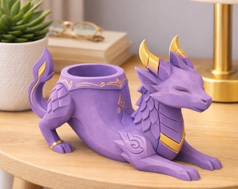 Può includere: Un vaso a forma di drago viola con dettagli dorati. Il drago è in posizione reclinata, con la testa appoggiata e gli occhi chiusi. Il vaso ha un'apertura circolare per le piante. Le corna e i dettagli decorativi del drago sono dorati.