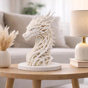 May include: A detailed, off-white dragon sculpture with intricate openwork design. The dragon is mounted on a round, white base. The sculpture is displayed on a wooden table, alongside a lamp and decorative vase.