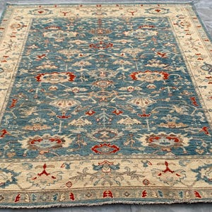 Könnte beinhalten: Ein rechteckiger, handgeknüpfter Teppich mit einem zentralen türkisfarbenen Feld und einem cremefarbenen Rand. Der Teppich weist ein kompliziertes Blumenmuster in Rot-, Beige- und Blautönen auf. Der Teppich liegt auf einer grauen Fliesenoberfläche.