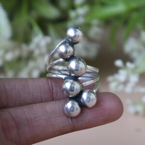 Peut inclure: Une bague en argent avec un design en spirale ornée de plusieurs petites sphères polies. L'anneau s'enroule autour du doigt, offrant une esthétique distinctive et contemporaine. Les sphères sont espacées uniformément.
