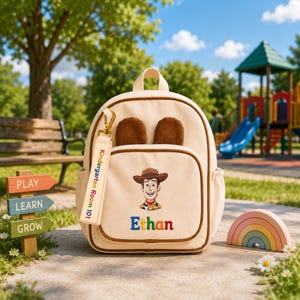 May include: A beige backpack featuring brown ears, an embroidered Woody character, and the name Ethan in colorful letters. A matching beige keychain tag is attached, printed with the text Kindergarten Room 101 in red and green lettering.