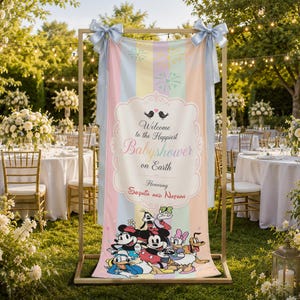 May include: A vertical fabric banner featuring pastel vertical stripes, light blue bows at the top, and a central decorative frame with the text Welcome to the Happiest Babyshower on Earth Honoring Sophia and Nathan, with Disney characters below.