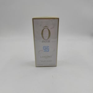 Può includere: Scatola di profumo rettangolare su sfondo bianco. La scatola presenta il testo "O d'AZUR" in oro, un motivo floreale blu e il marchio "Lancôme". La scatola contiene 50 ml di Eau de Toilette.