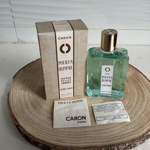 Può includere: Un flacone in vetro di dopobarba Caron Pour Un Homme con liquido verde chiaro e tappo dorato, accompagnato dalla scatola originale in cartone beige, un piccolo foglietto illustrativo bianco e un'etichetta rettangolare con testo nero.