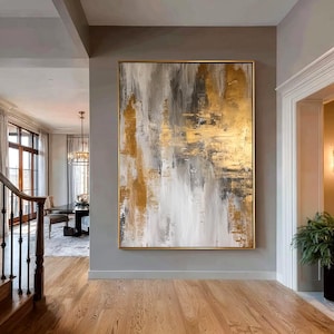 Peut inclure: Grande peinture abstraite avec des coups de pinceau dorés, gris et blancs dans un cadre doré. L'œuvre est accrochée à un mur gris dans un couloir bien éclairé avec des planchers de bois franc. La texture et la palette de couleurs créent une esthétique moderne.