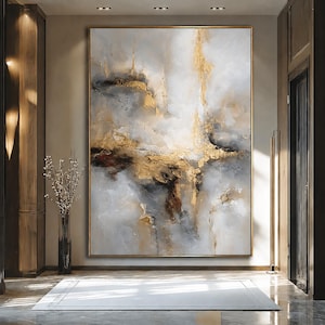 May include: A large rectangular abstract painting featuring a textured composition of white, gray, and black tones accented with metallic gold leaf. The artwork is framed in a thin gold border and displays thick, layered paint strokes throughout.