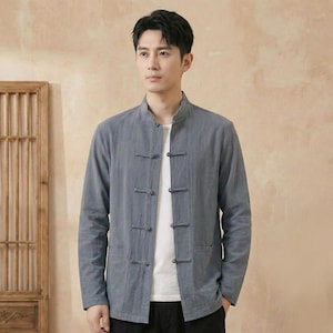 Peut inclure: Une veste grise à manches longues avec un col mao et des fermetures à brandebourgs. La veste a deux poches avant et est portée sur une chemise blanche. Le style rappelle les vêtements asiatiques traditionnels.