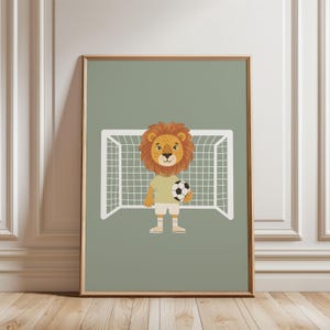 May include: A framed illustration of a cartoon lion in a football uniform holding a football. The lion has a tan body, a yellow shirt, and white shorts. A white football goal is behind the lion against a sage green background.