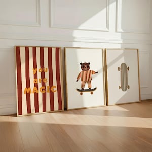 Puede incluir: Tres l&aacute;minas decorativas enmarcadas. La primera presenta rayas verticales de color rojo oscuro y crema con el texto "you are MAGIC" en naranja. La segunda muestra un oso pardo en pijama de rayas sobre un monopat&iacute;n. La tercera muestra un monopat&iacute;n.