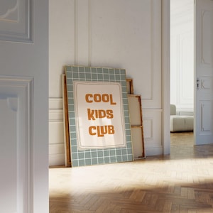 Puede incluir: Un cuadro decorativo rectangular con un fondo de patr&oacute;n de cuadr&iacute;cula en color verde salvia y una forma rectangular central de color crema. El texto COOL KIDS CLUB est&aacute; impreso en una fuente sans-serif redondeada, negrita y naranja.