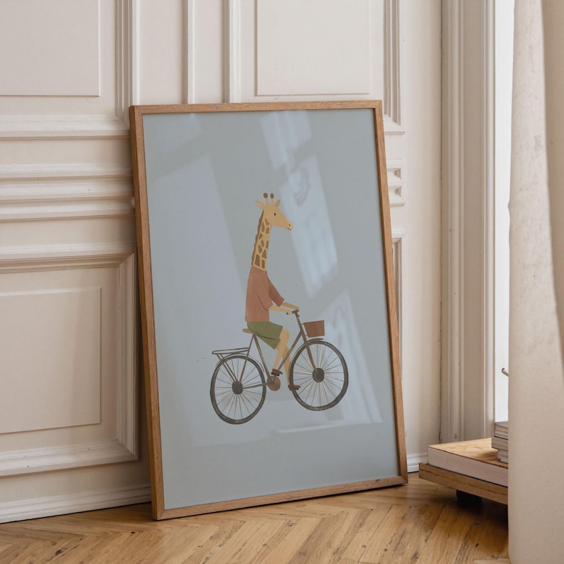 Puede incluir: Una l&aacute;mina enmarcada con una ilustraci&oacute;n estilizada de una jirafa con camiseta marr&oacute;n y pantalones cortos verdes montada en una bicicleta negra con una peque&ntilde;a cesta delantera, sobre un fondo azul gris&aacute;ceo claro.
