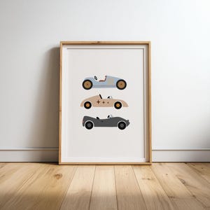 Puede incluir: Una l&aacute;mina enmarcada con tres coches de carreras vintage estilizados apilados verticalmente. El coche superior es azul claro, el central es beige con estrellas y el inferior es gris oscuro. Cada coche tiene un dise&ntilde;o de cabina abierta.