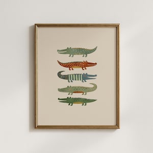 Puede incluir: Una l&aacute;mina de arte enmarcada que muestra cinco cocodrilos apilados en fila. Los cocodrilos est&aacute;n ilustrados en varios colores, incluyendo verde, naranja y azul, con patrones de rayas y puntos sobre un fondo de color beige claro s&oacute;lido.