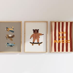 Puede incluir: Tres l&aacute;minas decorativas enmarcadas. La de la izquierda muestra tres aviones peque&ntilde;os en azul, marr&oacute;n y azul claro. La central presenta un oso marr&oacute;n en pijama de rayas sobre un monopat&iacute;n. La de la derecha tiene rayas rojas y el texto you are MAGIC.