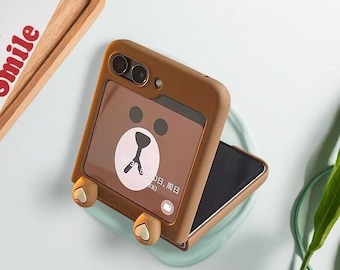 May include: A brown phone case with a bear design. The case has a bear face on the front and bear paw details at the bottom. The phone screen displays the time and date. The case is open, revealing the phone's screen.