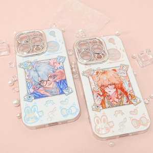 Puede incluir: Dos fundas blancas para teléfono con protectores de lente de cámara transparentes. Cada funda presenta un retrato de personaje de estilo anime colorido. Una tiene el pelo azul, la otra naranja. Ambas fundas tienen patrones decorativos de conejitos, lazos y notas musicales.