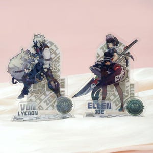 Peut inclure: Deux présentoirs acryliques pour personnages avec des illustrations de style anime. L'un représente Von Lycaon avec un loup, l'autre Ellen Joe. Les deux présentoirs ont des bases décoratives avec du texte et des logos.