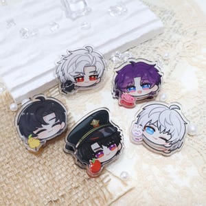 Puede incluir: Colección de cinco colgantes acrílicos con diseños de personajes estilo anime. Cada colgante muestra un personaje diferente con colores de pelo, atuendos y accesorios únicos, incluyendo un sombrero, fruta y un conejito. Los colgantes son transparentes con ilustraciones coloridas.