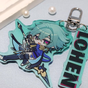 May include: An acrylic keychain featuring a stylized anime character with teal hair, wearing a blue and black outfit, holding a spear. The charm is attached to a silver metal clasp and includes a rectangular tag with the text LOHEN in black letters.