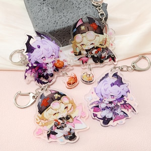 May include: A selection of anime-style acrylic keyrings featuring colourful characters with wings and horns. Each keyring has a silver ring. The characters wear various outfits and accessories, including glasses and hats.
