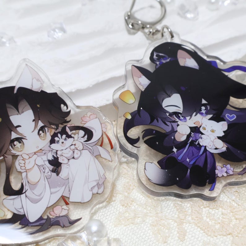 May include: Two clear acrylic keychains featuring anime-style characters with animal ears. One keychain shows a character in white holding a husky puppy, the other shows a character in purple holding a white cat. Both have floral accents.