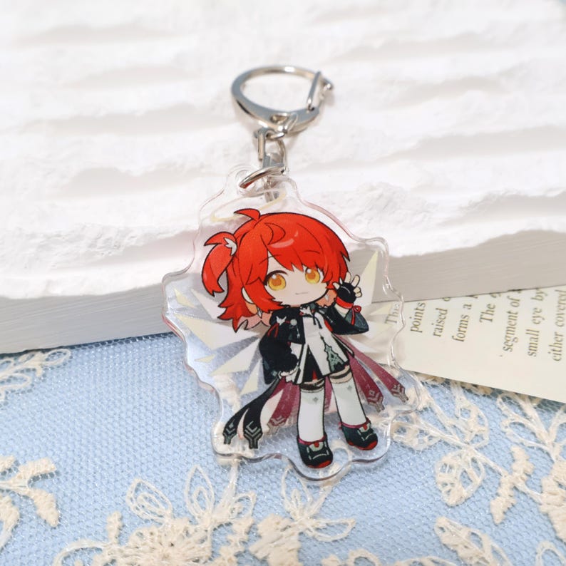 May include: A clear acrylic keychain featuring a cartoon character with red hair, black and white clothing, and a silver keyring. The character is on a clear, star-shaped background.