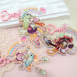 May include: A collection of acrylic keychains featuring colorful anime-style angel characters. Each keychain has a pink heart-shaped clasp and the word "ANGELS" in a rainbow gradient. The angel characters have wings and are in various poses.