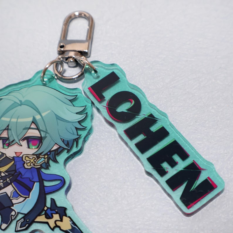 May include: An acrylic keychain featuring a stylized anime character with mint green hair and a blue outfit, attached to a silver metal lobster clasp. A rectangular mint green acrylic tag with the black text LOHEN is attached to the same clasp.