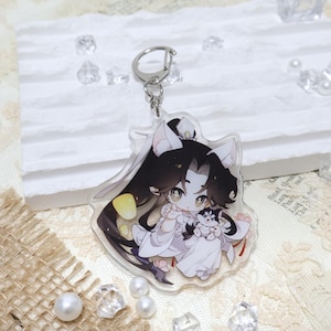 May include: A clear acrylic keychain featuring a cartoon character with long black hair, white clothing, and a small dog. The keychain has a silver metal ring for attachment.