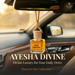May include: A car air freshener with a clear glass bottle and a wooden cap, hanging from a string. The label reads "Car Freshner Amber Vanilla Bliss." The image also displays the text "AYESHA DIVINE" and "Divine Luxury for Your Daily Drive."