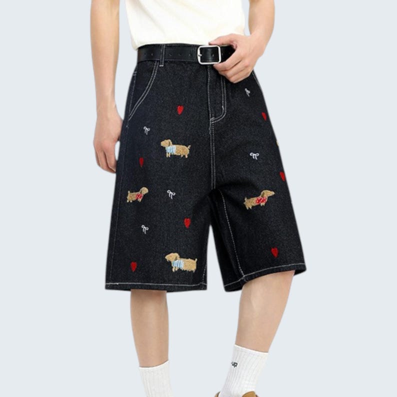 May include: Black denim shorts with white stitching, a black belt, and embroidered dachshund dogs and red hearts. The shorts have a classic five-pocket design and a button and zipper closure.
