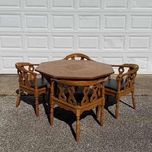 May include: A wooden dining set consisting of an octagonal table and four chairs. Each chair features a curved backrest with a decorative cutout pattern and a black upholstered seat. The table has a flat octagonal top and four sturdy legs.