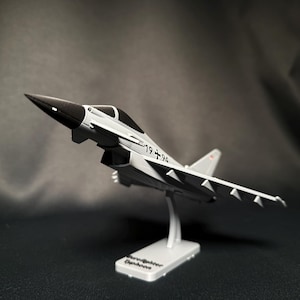 Może przedstawiać: Model samolotu bojowego Eurofighter Typhoon w kolorze szarym i czarnym, zamontowany na stojaku. Model ma numer "19+94" i jest prezentowany na podstawie z napisem "Eurofighter Typhoon".