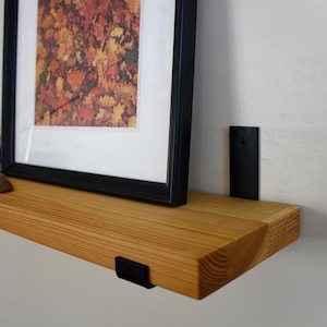 May include: A wooden floating shelf with black metal brackets. A framed picture with fall foliage art, a candle, incense, and a wooden incense holder are on the shelf. The shelf is approximately 76 cm long.